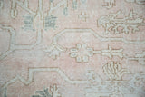 Distressed Oushak rug detail: blush field, ivory geometric patterns, and subtle gray-green vines.