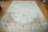 Distressed Oushak carpet corner, soft sea foam green, coffee bean floral patterns.