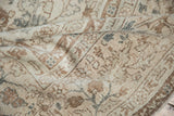 Folded Oushak rug highlighting distressed pile and faded floral motifs in ivory, beige, and bronze.
