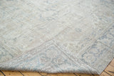 Folded corner of a distressed Oushak rug, revealing its backing and muted grey patterns.
