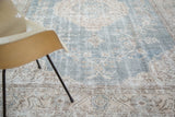 Distressed Oushak carpet, showing faded slate blue, ivory, and beige floral designs.