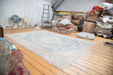 Faded slate blue Oushak rug with distressed texture and intricate ivory floral patterns.