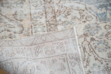 Folded distressed Oushak carpet revealing soft, muted pile and hand-knotted back.