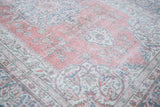 Distressed Oushak rug corner with faded raspberry red, ivory, and deep sky blue curvilinear motifs.