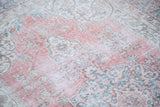 Distressed Oushak rug showing faded raspberry red and deep sky blue curvilinear patterns.