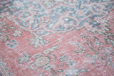 Distressed Oushak rug showing faded raspberry red, ivory, and deep sky blue curvilinear motifs.