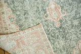 Distressed Oushak rug's corner with textured green field and terra cotta palmette border.