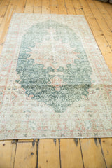 Distressed Oushak rug corner with worn pile, forest green field, and palmette border.
