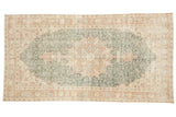 Distressed Oushak rug, time-softened forest green field, peach medallion, terra cotta border.