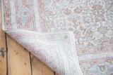 Folded distressed Oushak carpet, showing hand-knotted weave and faded ivory, blush, slate green.