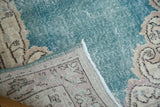 Distressed Oushak runner close-up: worn aqua blue pile, ornate ivory foundation, and delicate fringe.