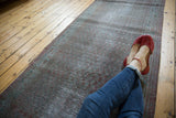 Distressed texture of vintage overdyed runner with muted red and faded teal geometric border.
