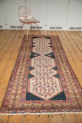 Distressed Malayer rug runner's stylized geometric border in beige, red, and navy with fringe.