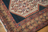 Distressed geometric Malayer rug corner, showing navy field, beige border, and intricate patterns.