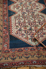 Distressed Malayer runner featuring geometric stylized patterns in faded cinnabar red and navy.
