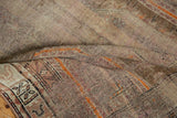 Folded distressed Caucasian runner showing geometric designs in brown, ivory, and bright orange.