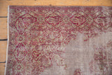 The distressed corner of a Turkish Sivas rug showing the cranberry floral border and exposed white foundation.
