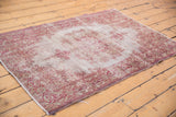 Angled view of a distressed Sivas rug with a faded center and cranberry red floral border.
