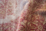 Worn pile of a distressed Turkish rug showing the grey foundation beneath cranberry red motifs.