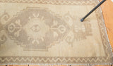 Bottom corner of vintage Oushak rug, displaying soft beige pile and zigzag border.