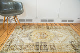 Distressed Oushak rug's muted ivory, brown, and green tones with geometric and vine motifs.