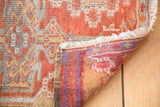 Vintage Oushak rug folded, showing fringed edge, red pile, and vibrant purple-orange hand-knotted reverse.