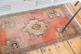 Distressed Oushak rug mat corner showing faded orange field, meandering border, and fringe.