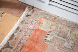 Distressed Oushak rug corner with faded orange pile, muted grey patterns, and white fringe.