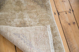 Distressed Oushak rug texture in neutral tones, showing hand-knotted back and fringe.