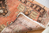 Folded corner of vintage Oushak rug, showing cinnabar field, patterned borders, and hand-knotted reverse.