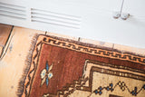 Vintage Oushak rug corner with deep copper pile, tangerine border, and fringe.