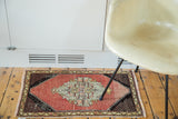 Distressed Oushak rug with a cinnabar red field, grey medallion, and patterned black spandrels.