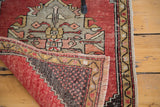 Distressed Oushak rug corner revealing hand-knotted back, cinnabar field, diamond medallion, and fringe.