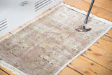 Distressed Oushak rug mat's low pile, subtle mauve field, and dark design with fringe.