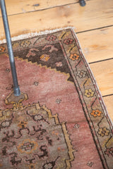 Decorative Oushak rug mat with distressed mauve field, stepped spandrels, and scrolling floral border.