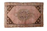 Distressed Oushak mat with a mauve field, silver charcoal medallion, and floral border.