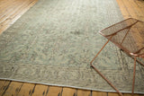 Distressed Oushak carpet edge, textured pile, faded green and grey floral patterns.