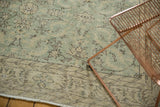 Distressed Oushak rug corner, soft green and ivory floral arrangements with geometric border.