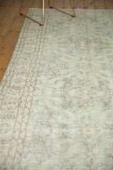 Distressed vintage Oushak carpet border showing curved vines and soft green floral field.