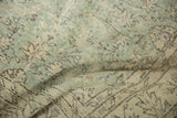 Distressed Oushak carpet texture with time-softened green and ivory floral patterns.