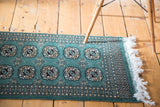 Ivory fringe and geometric border details on a forest green vintage Bokhara rug.