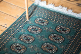 Forest green Bokhara rug with intricate double column guls and ivory fringe.