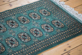 Forest green Bokhara rug with elephant footprint guls, intricate borders, and white fringe.