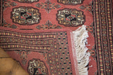 Vintage Bokhara rug folded, showing deep blush elephant footprint guls, intricate borders, and ivory fringe.