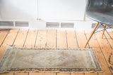 Distressed Oushak mat with faded mauve, celadon, and ivory tones.