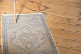 Distressed hand-knotted Oushak rug mat corner showing grey geometric patterns on faded sandalwood.