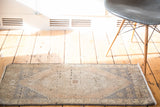 Distressed Oushak rug mat with faded peach field, slate blue geometric motifs, charcoal edge.