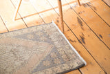 Distressed corner of an Oushak rug with faded peach, ivory, and slate gray colors.