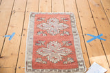 Distressed brick red Oushak rug corner with partial quatrefoil medallion and faded floral bursts.