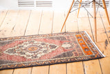 Geometric tangerine border and curvilinear motifs on vintage Oushak rug end, with fringe.